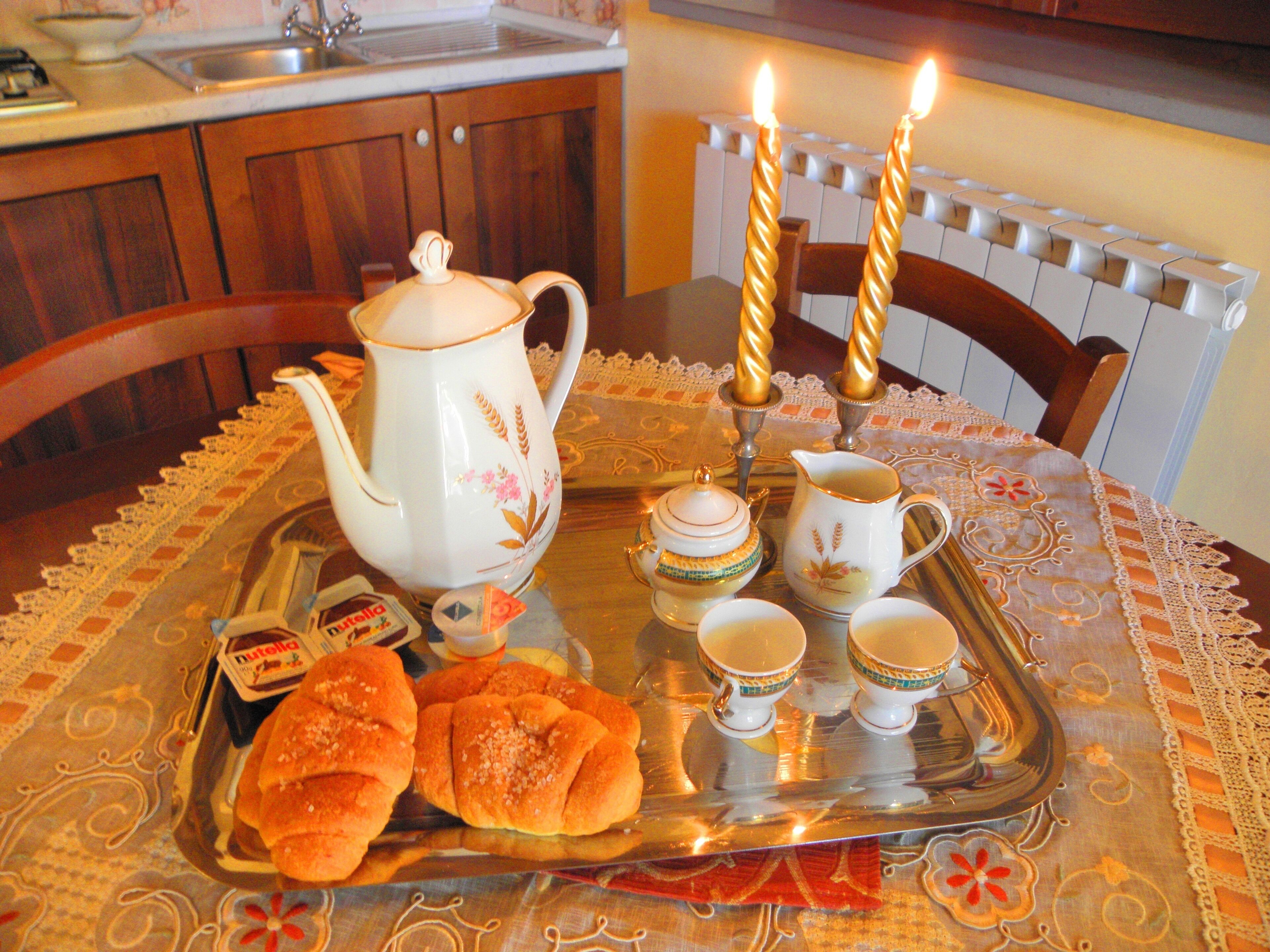 A tray with pastries, a teapot, cups, and a candle holder on a table with a lace tablecloth.