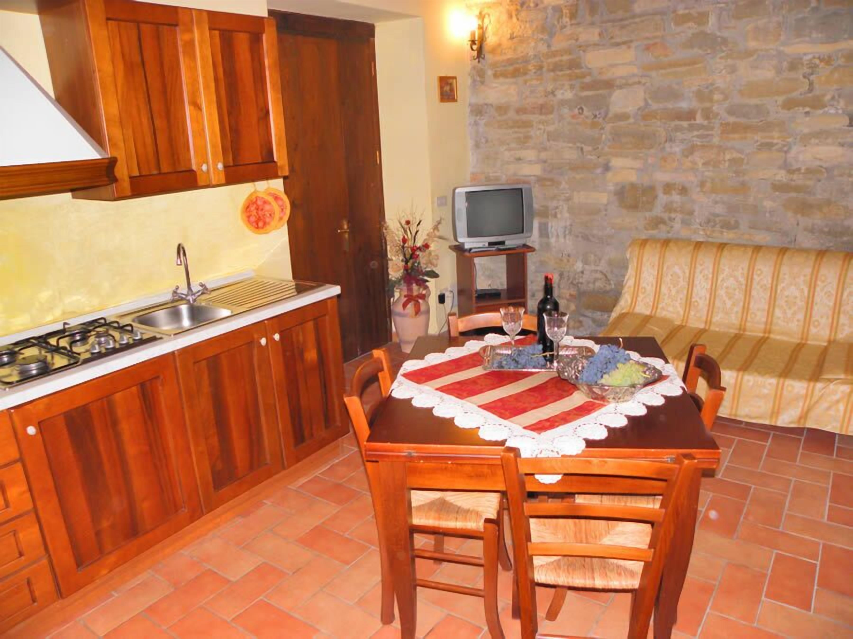 A compact kitchen with wooden cabinets, a gas stove, and a sink. There's a dining table with chairs and a small television on a stand.