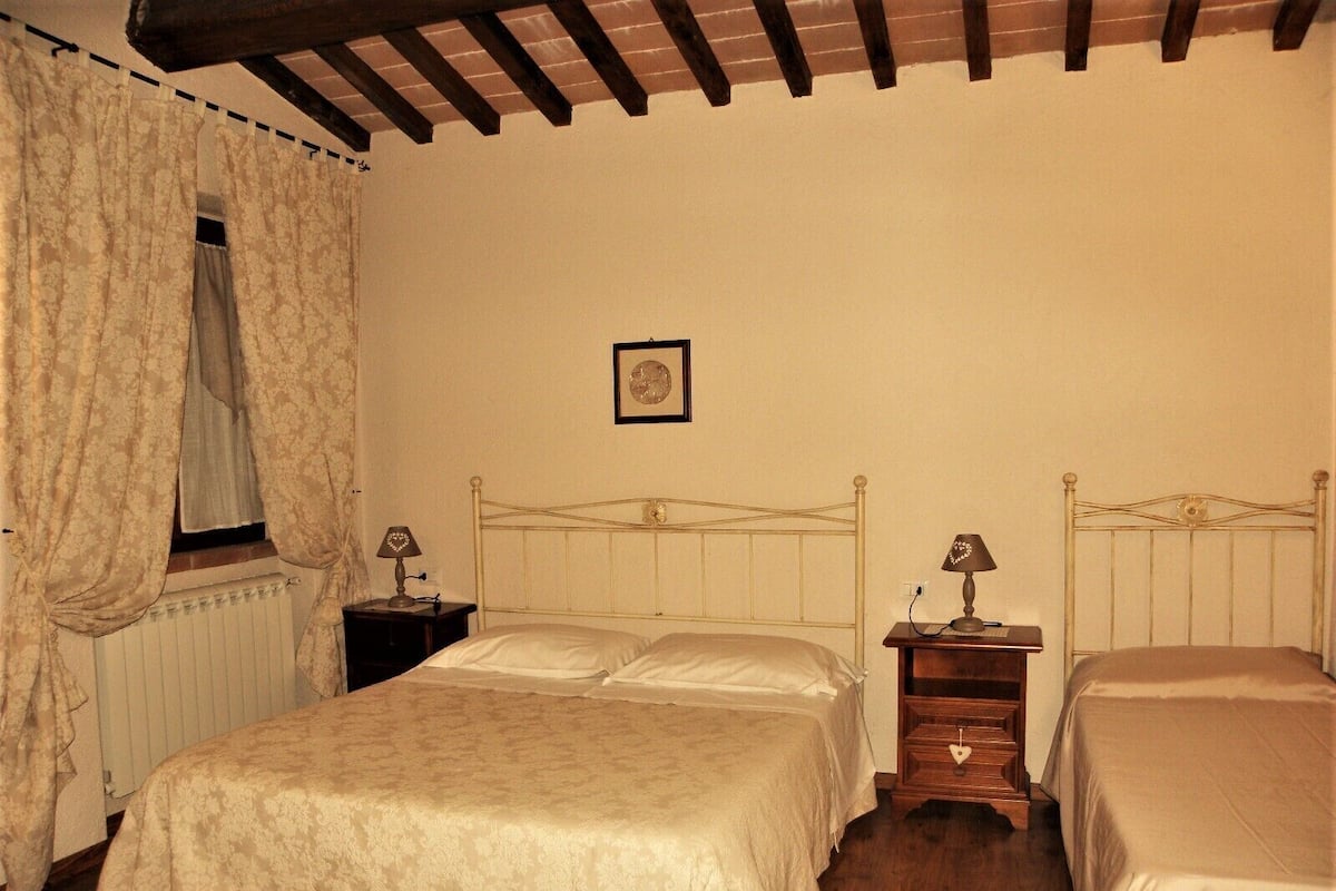 Un dormitorio con una cama grande, dos mesitas de noche, una ventana con cortinas y un cuadro en la pared.