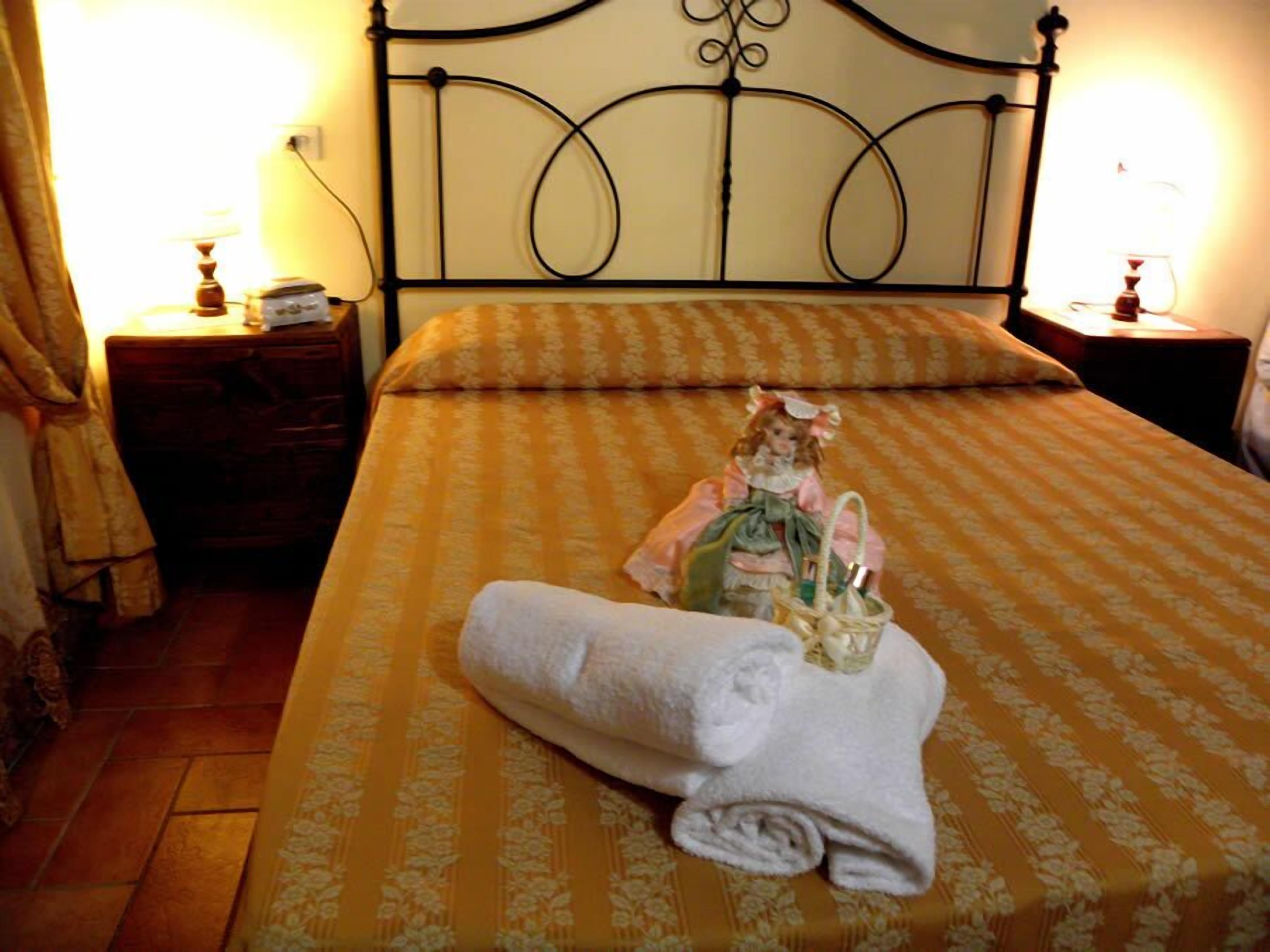 Una cama bien hecha con una colcha estampada de flores, una toalla blanca enrollada y un objeto decorativo sobre la cama.