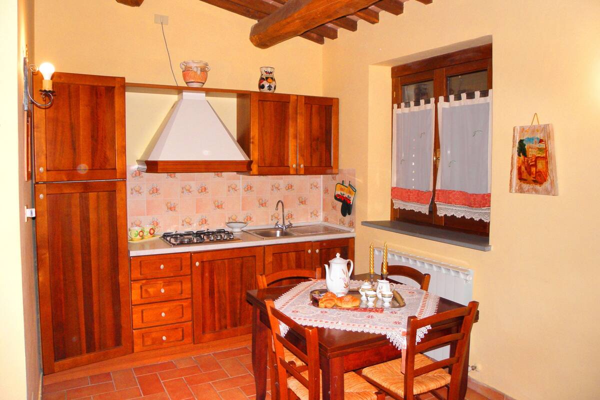Una cocina con armarios de madera, estufa a gas, un lavabo y una mesa de comedor con sillas.