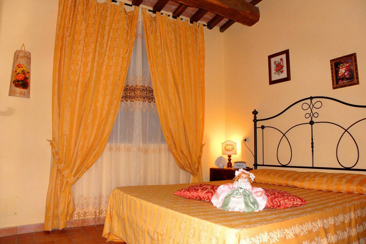 Un dormitorio con cama, cortinas, mesita de noche y adornos en la pared.