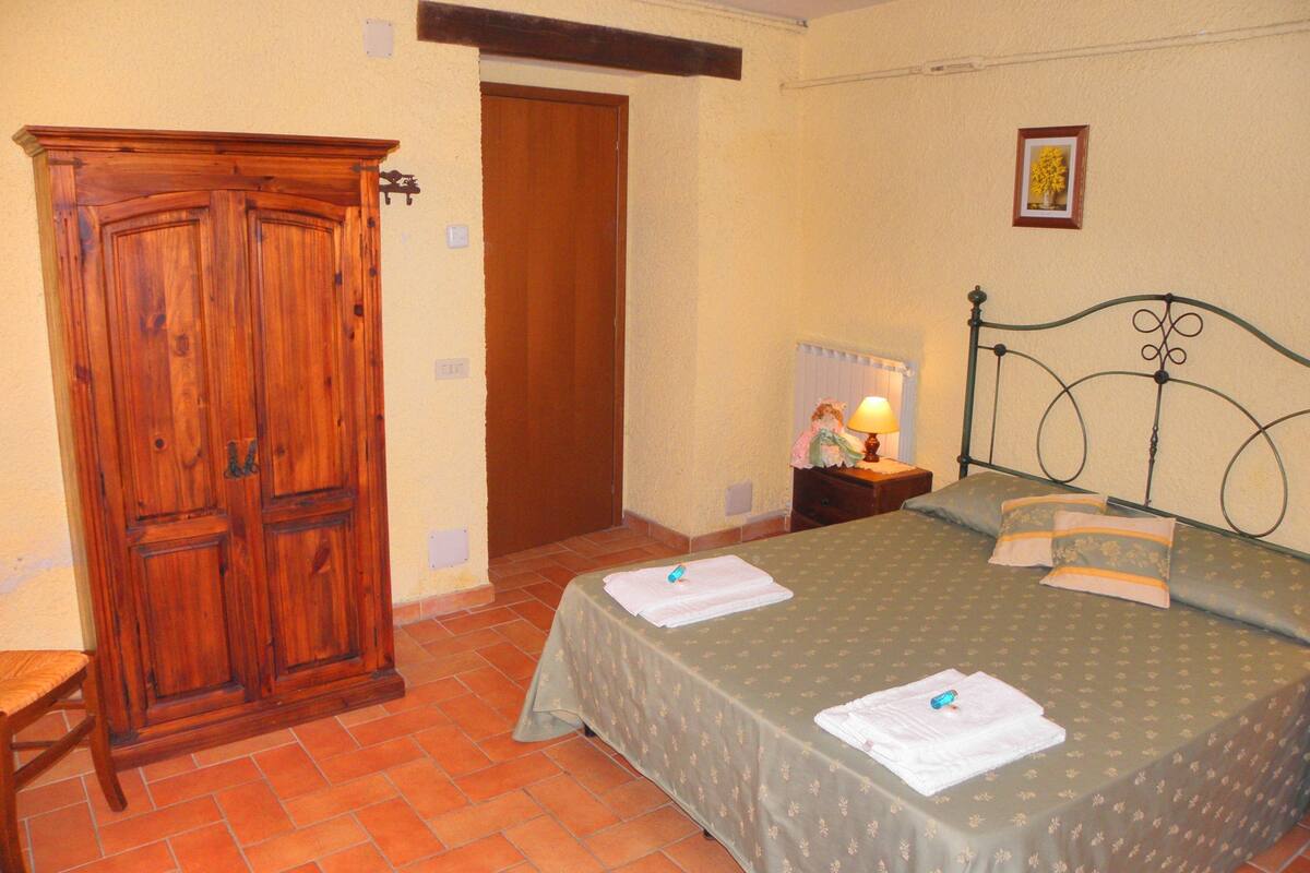 Un dormitorio con un armario de madera, una cama con cubrecama verde y una mesita de noche con lámpara.