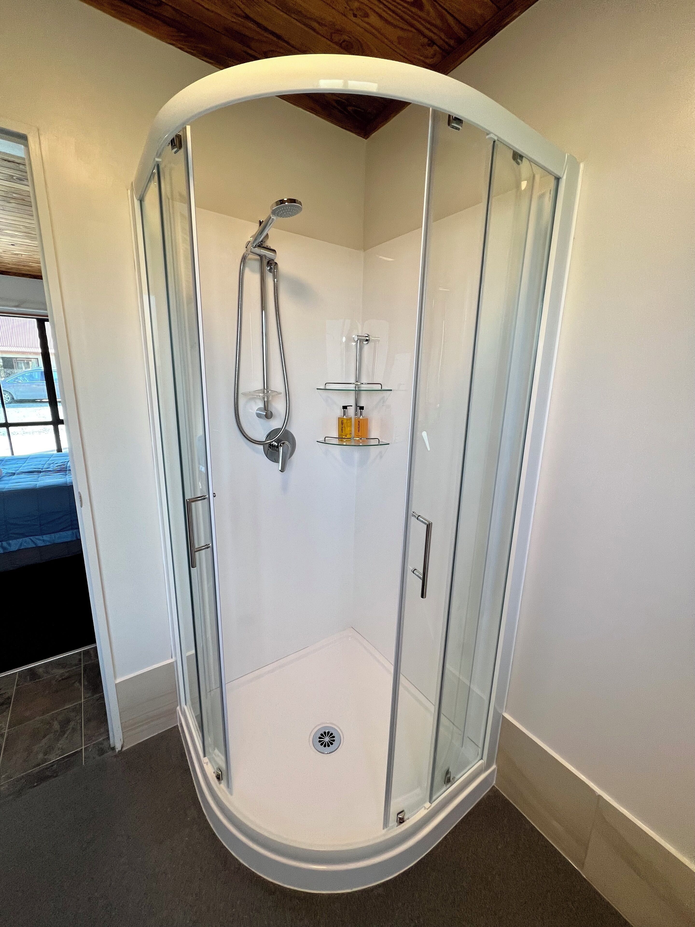 A glass-enclosed shower with a showerhead and a glass shelf with toiletries.