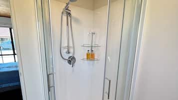 A glass-enclosed shower with a showerhead and a glass shelf with toiletries.