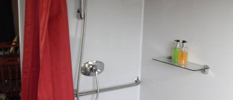 A shower with a red curtain, a glass shelf with toiletries, and a towel rack.