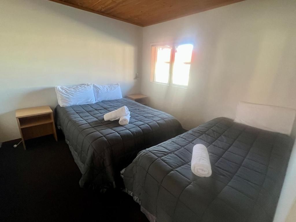 A small, simple room with two single beds, a nightstand, and a window.