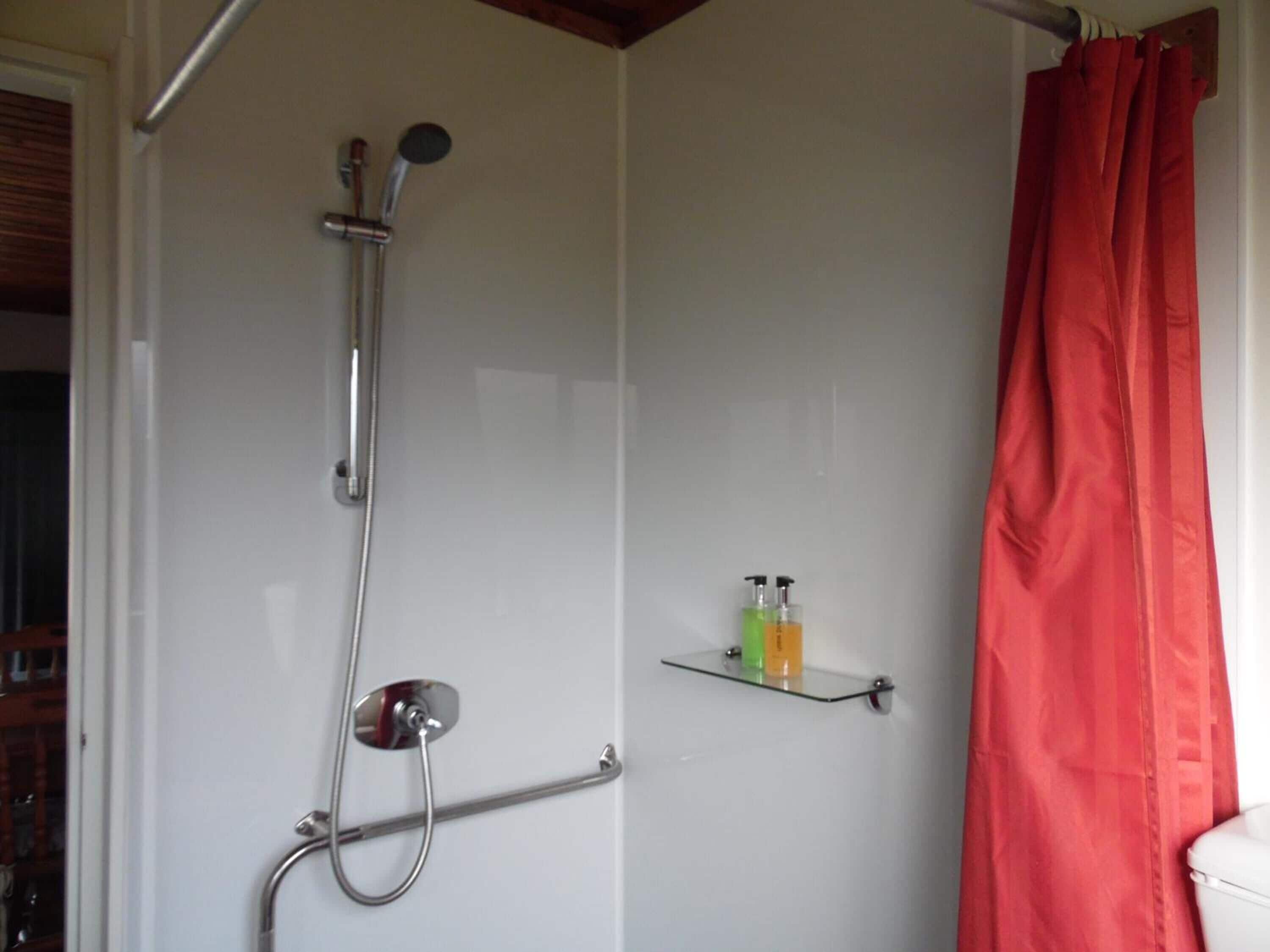 A shower with a handheld showerhead, a handheld shower attachment, and a glass shelf with toiletries.