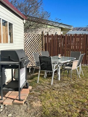 Un patio al aire libre con una parrilla, una mesa y sillas.