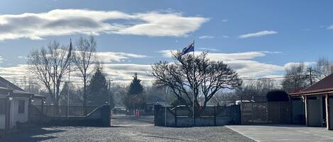 A paved courtyard with a flagpole, a building with a brown roof, and leafless trees.