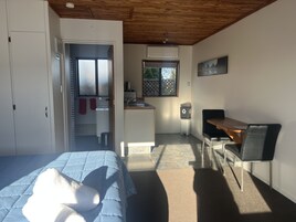 Un dormitorio con cama, techo de madera, kitchenette con lavamanos y zona de comedor con mesa y silla.