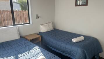 Une chambre avec deux lits, chacun recouvert d’une courtepointe bleue matelassée et agrémenté d’un oreiller blanc. Une table de chevet en bois se trouve entre les deux lits, et un tableau encadré est accroché au mur.