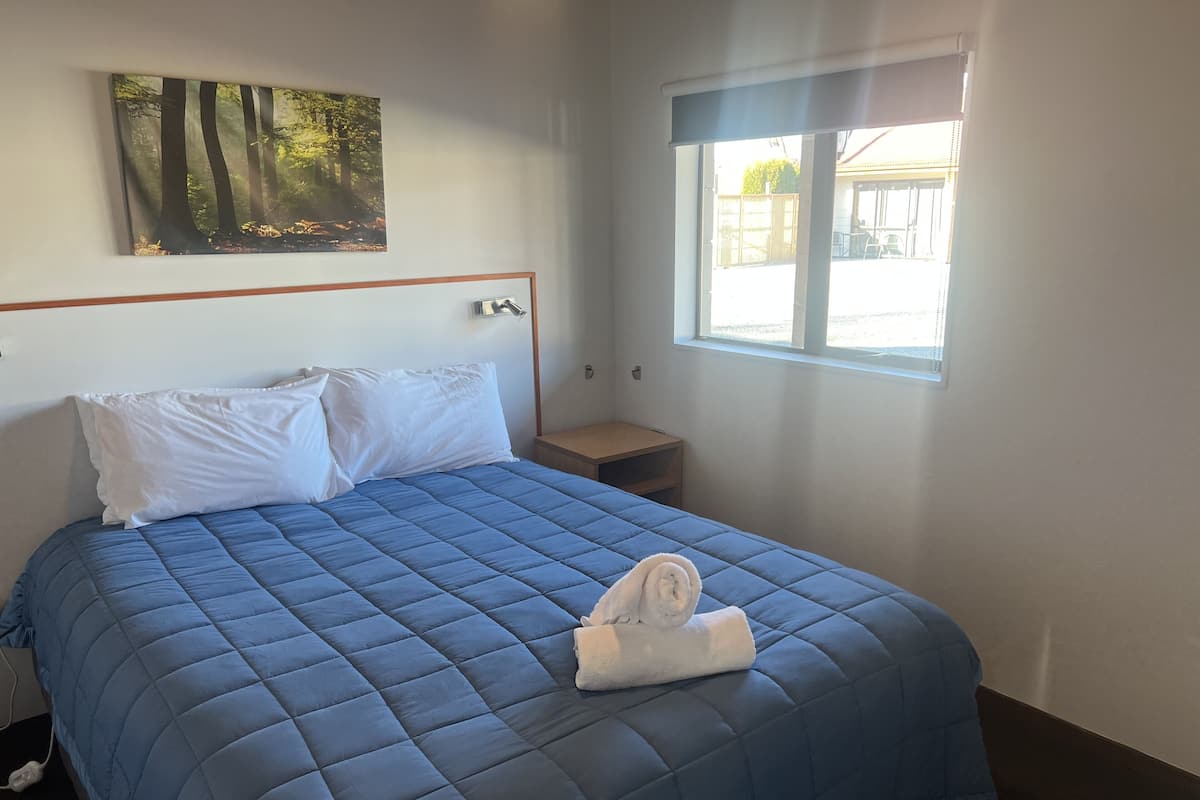 A neatly made bed with a blue quilt, white pillows, and a folded towel on the footboard.