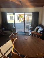 A room with a wooden table and chairs, a leather sofa, and a view through a glass door to an outdoor area with a patio and a fence.