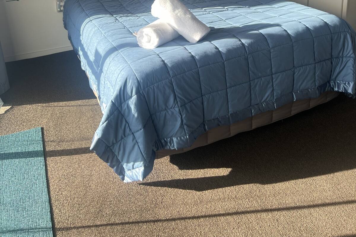 A bedroom with a bed, white pillows, a blue quilted bedspread, and a framed picture on the wall.