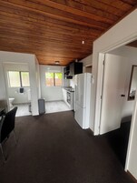 Una cocina compacta con electrodomésticos blancos, techo de madera y vistas al exterior por una ventana.