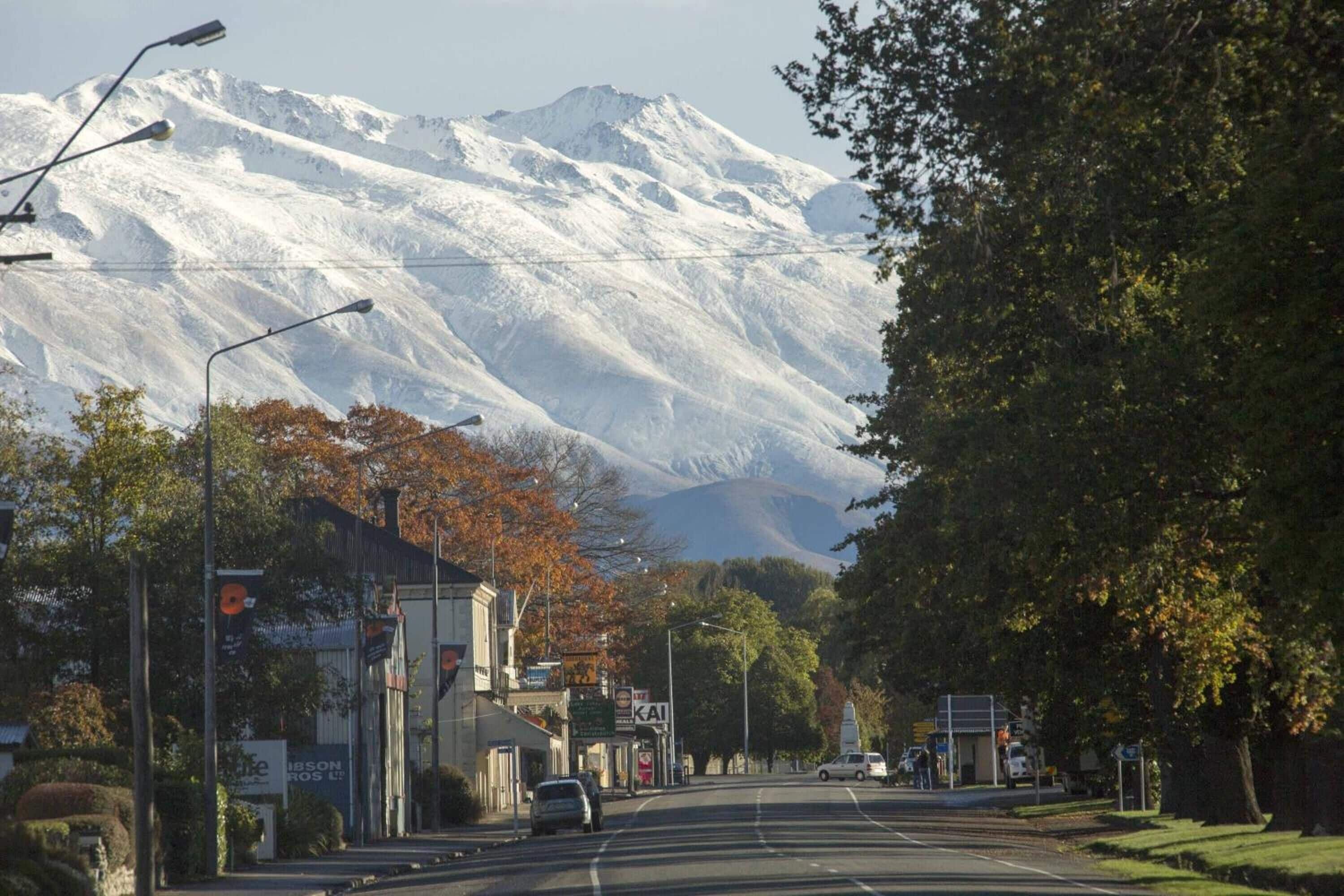 Eine Straße mit Gebäuden, ein Berg im Hintergrund und Bäume mit Herbstlaub.