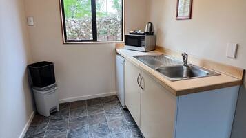 A compact kitchen with a window, a microwave, a sink, and a trash bin.