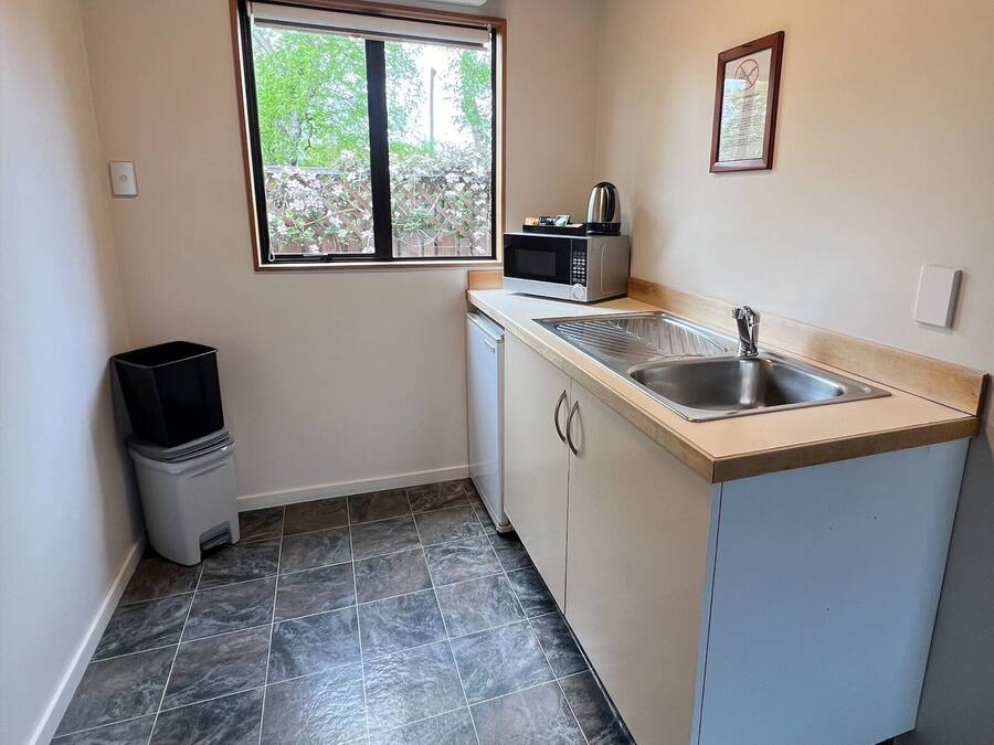 A compact kitchen with a window, a microwave, a sink, and a trash bin.