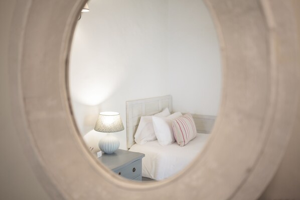 A bedroom with a bed, nightstand, lamp, and a mirror reflecting the room.