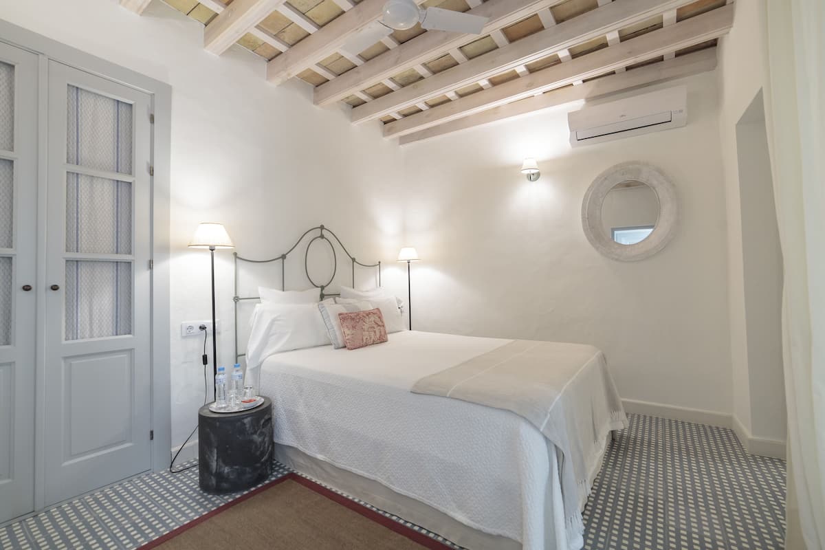 Une chambre à coucher avec un lit, des lampes de chevet, un miroir rond et un ventilateur de plafond.