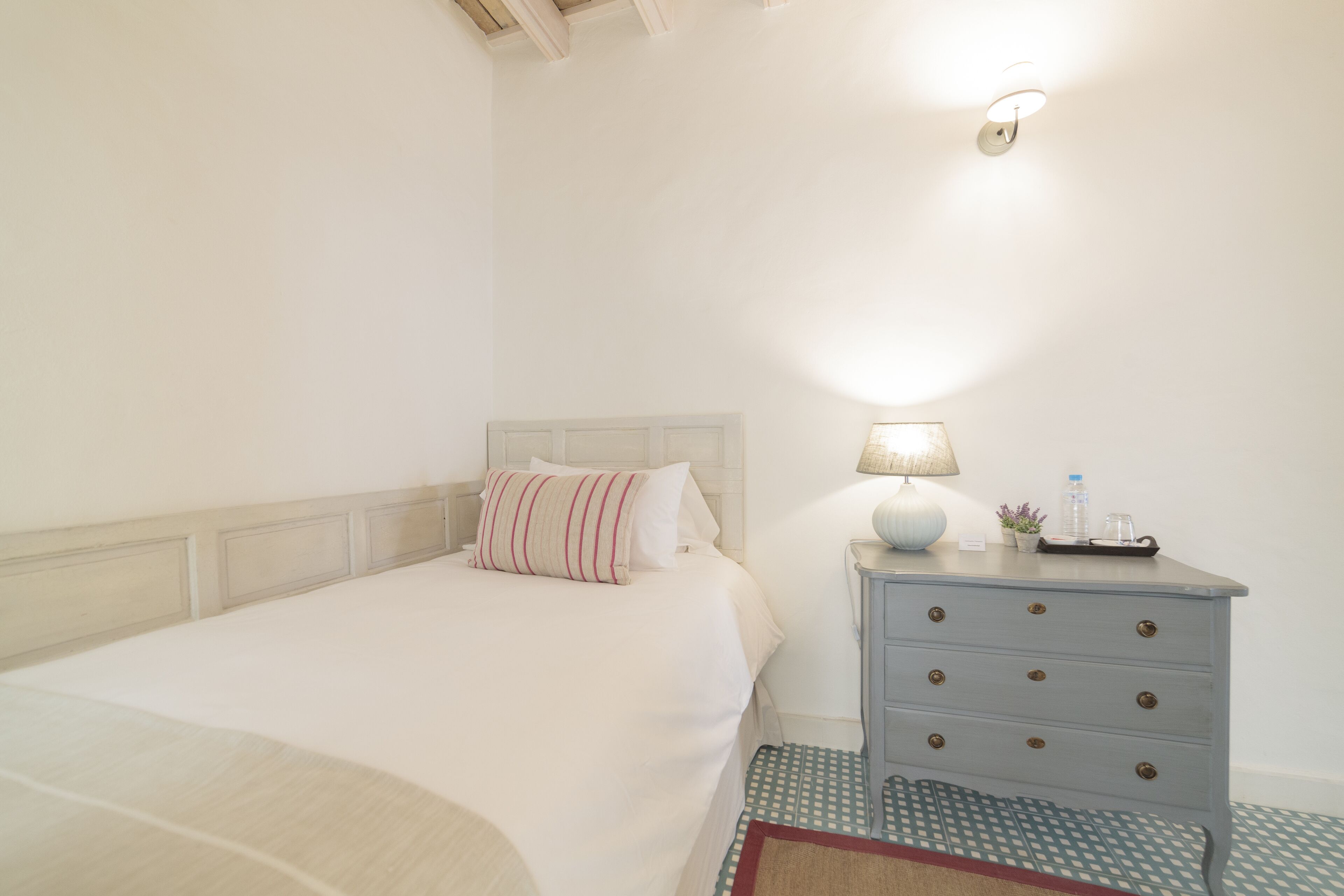 A neatly made bed with a striped pillow, a bedside table with a lamp, and a small plant.
