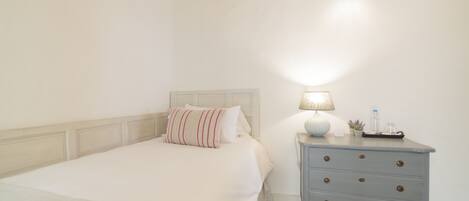 A neatly made bed with a striped pillow, a bedside table with a lamp, and a small plant.