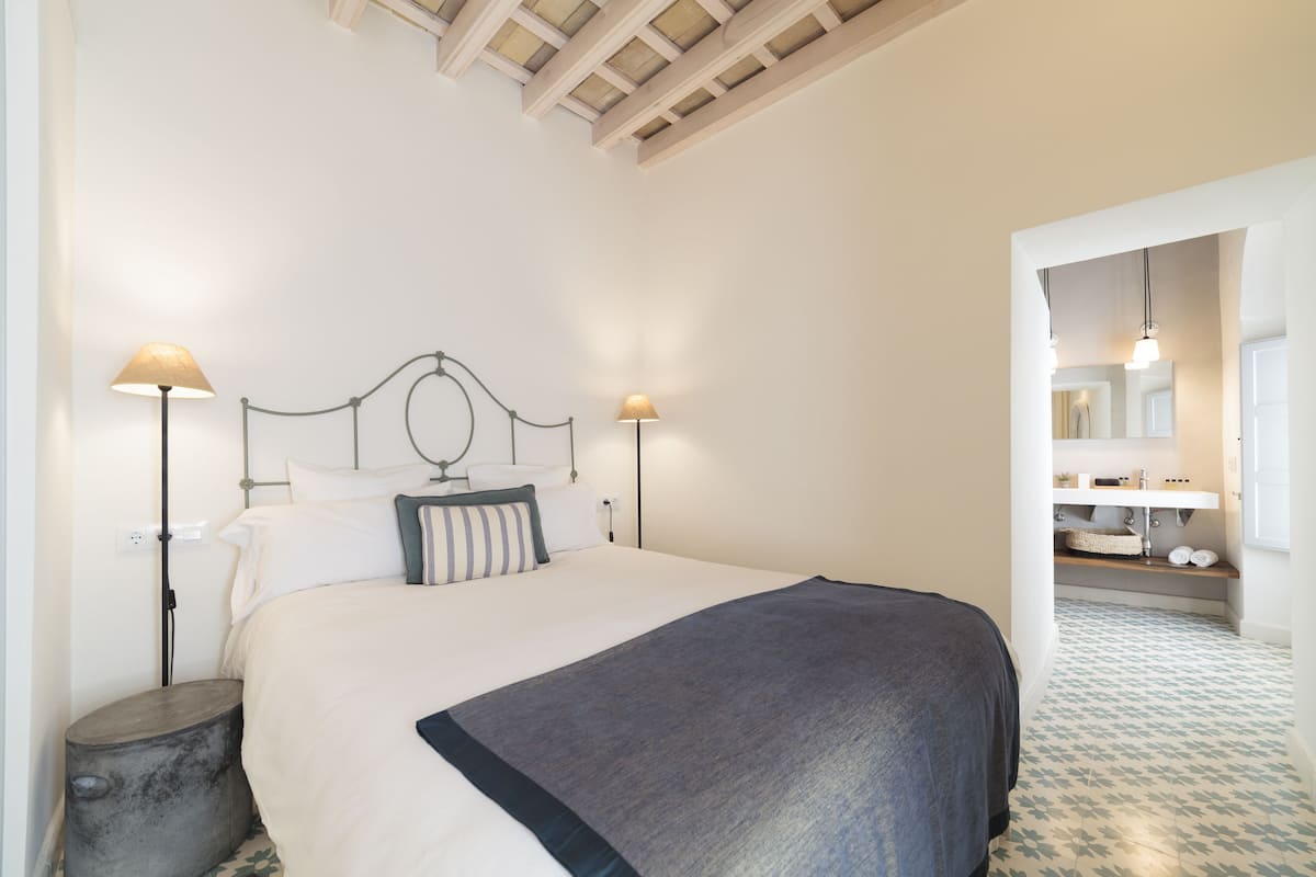 Une chambre bien rangée, avec un lit, des lampes de chevet et un coin salle de bain visible, comprenant un lavabo et un miroir.