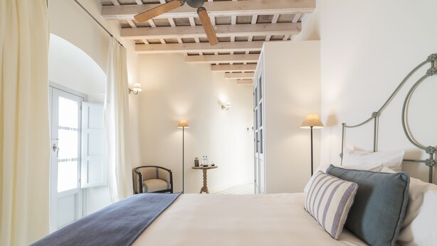 Ein Schlafzimmer mit einem großen Bett, einem Deckenventilator, einem Sessel und einem kleinen Tisch.