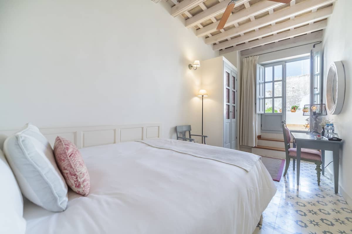Une chambre avec un grand lit, un bureau et une chaise. Il y a une fenêtre donnant sur l’extérieur.