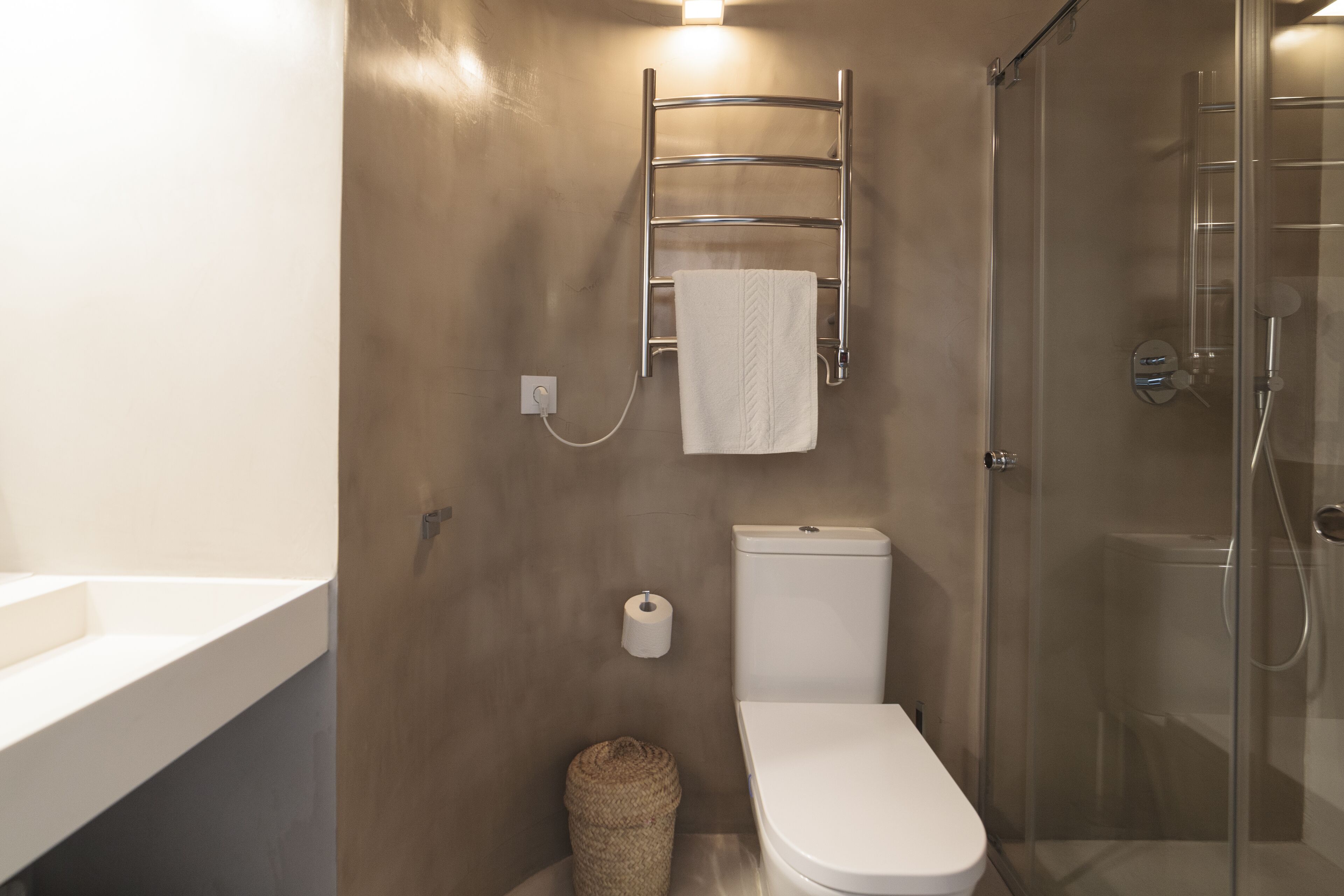 Un baño moderno con ducha de vidrio, inodoro blanco, toallero y un rollo de papel higiénico.