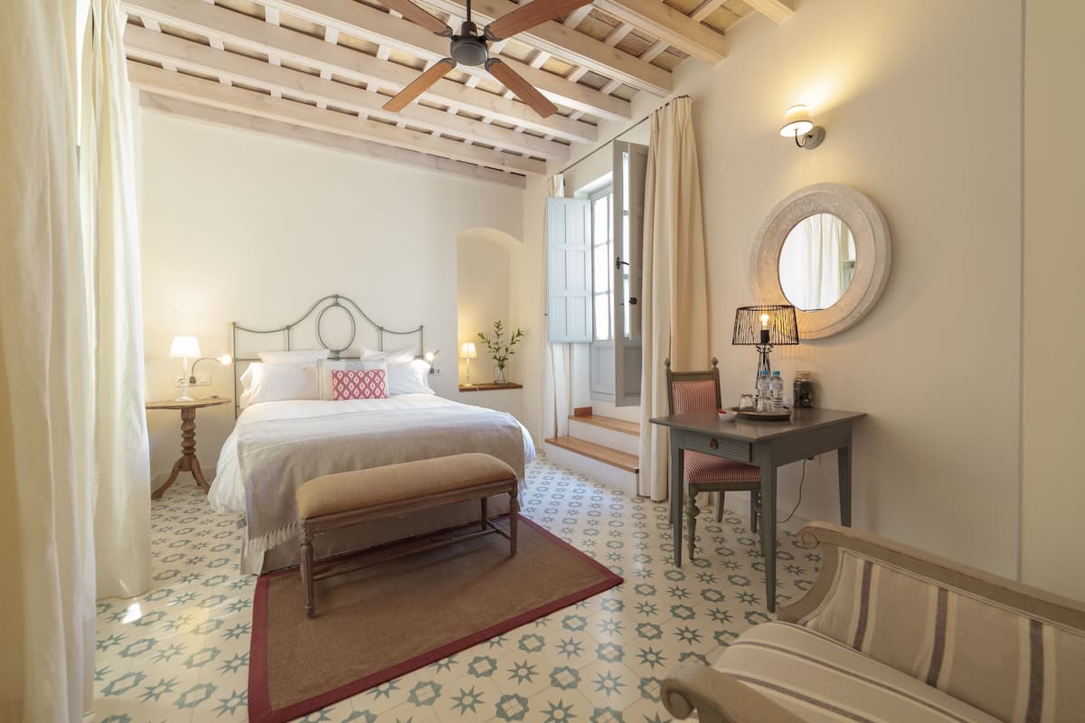 Une chambre à coucher comprenant un lit, un banc, une table de chevet, une lampe, un miroir et une vue sur l’extérieur.