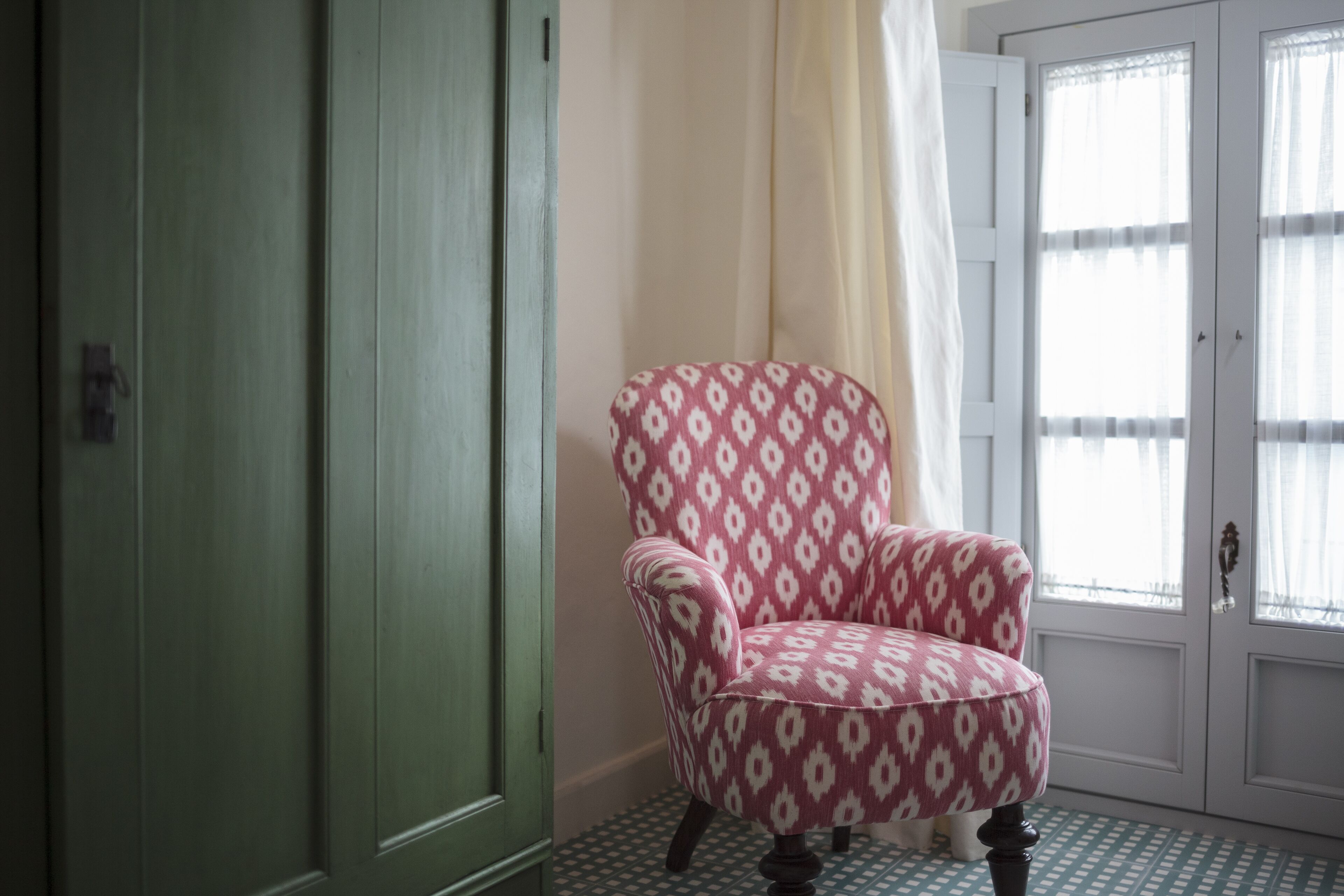 A room with a patterned armchair, a green door, and a window with sheer curtains.