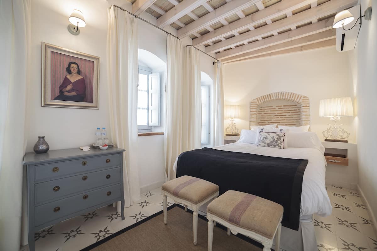 Une chambre à coucher avec un lit, une commode, un banc et un tableau au mur.