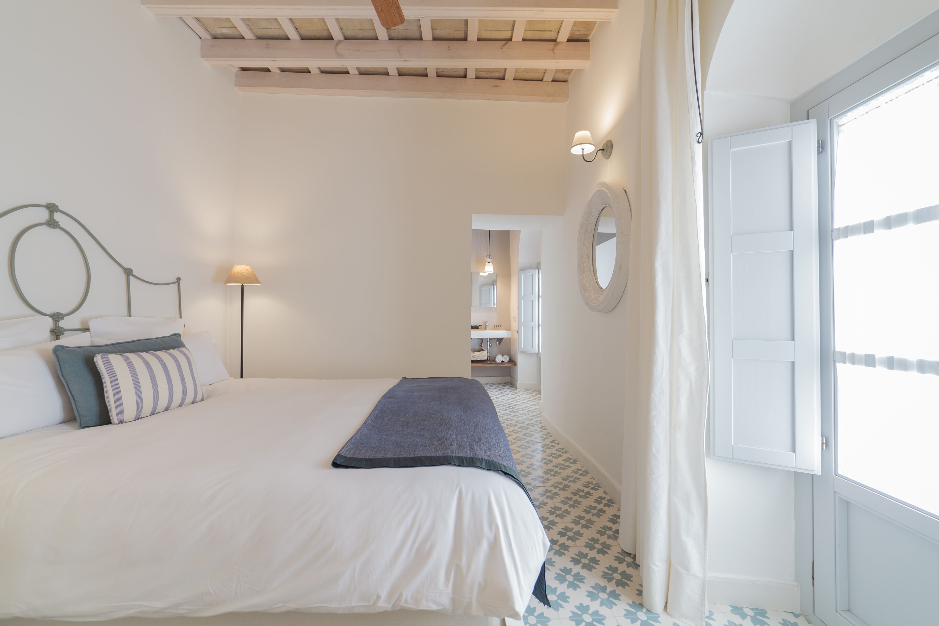 Un dormitorio con cama, una lámpara de noche, una ventana con cortinas y una puerta.