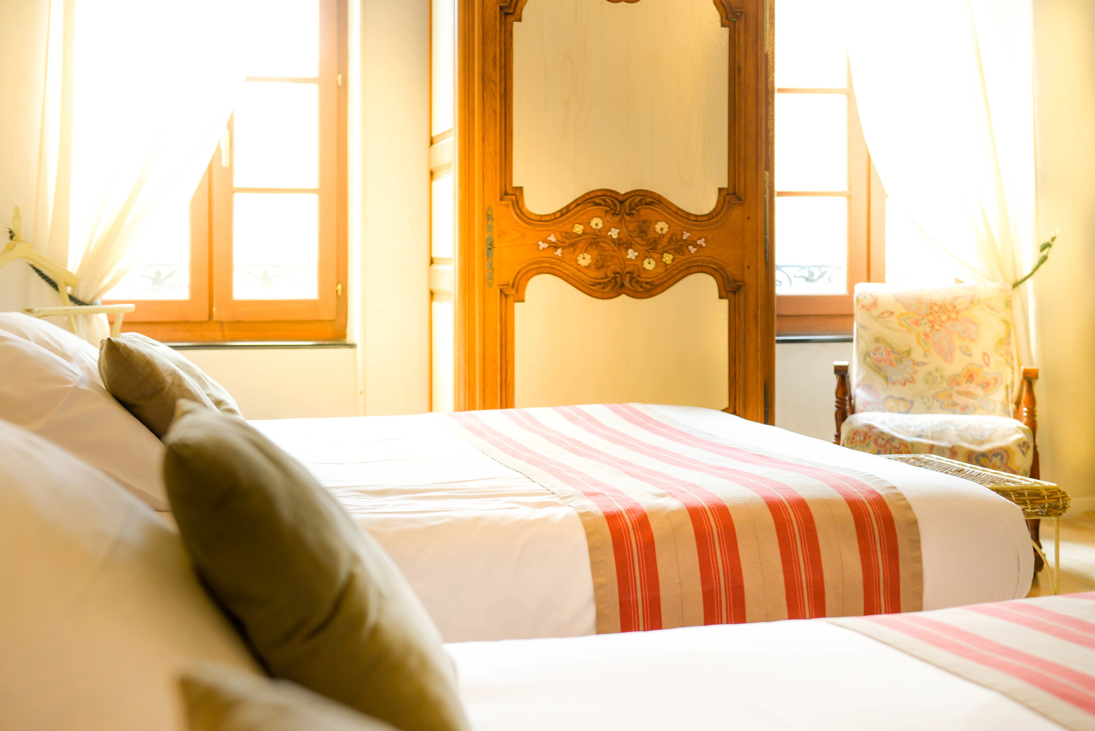 A hotel room with two beds, a wooden wardrobe, a chair, and a window with curtains.