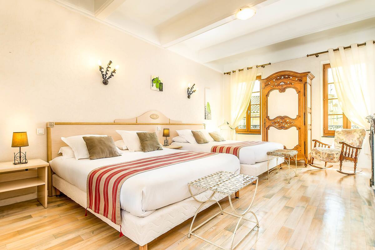 Une chambre d’hôtel avec deux lits, une armoire en bois, un fauteuil à bascule et une petite table.