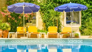 A pool area with two blue umbrellas, yellow lounge chairs, and a tiled pool edge. -  Logis Hôtel Restaurant Résidence (Nissan-lez-Enserune)