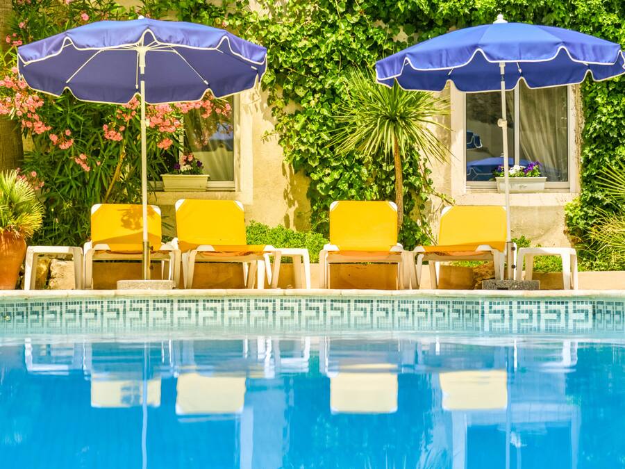 A pool area with two blue umbrellas, yellow lounge chairs, and a tiled pool edge.