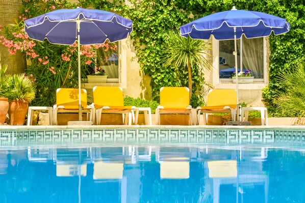 A pool area with two blue umbrellas, yellow lounge chairs, and a tiled pool edge.
