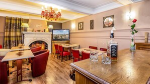 A hotel lobby with a fireplace, red chairs, a bar area, and a television mounted on the wall. -  Logis Hôtel Restaurant Résidence (Nissan-lez-Enserune)