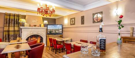 Un vestíbulo de hotel con chimenea, sillas rojas, zona de bar y un televisor en la pared.