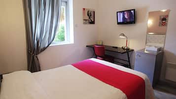 Habitación de hotel con cama, escritorio, silla, televisión y refrigerador pequeño.