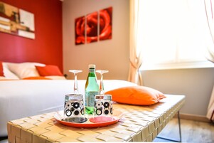 Una mesa ordenada con una botella, vasos y una bandeja en una habitación con cama y pared roja.