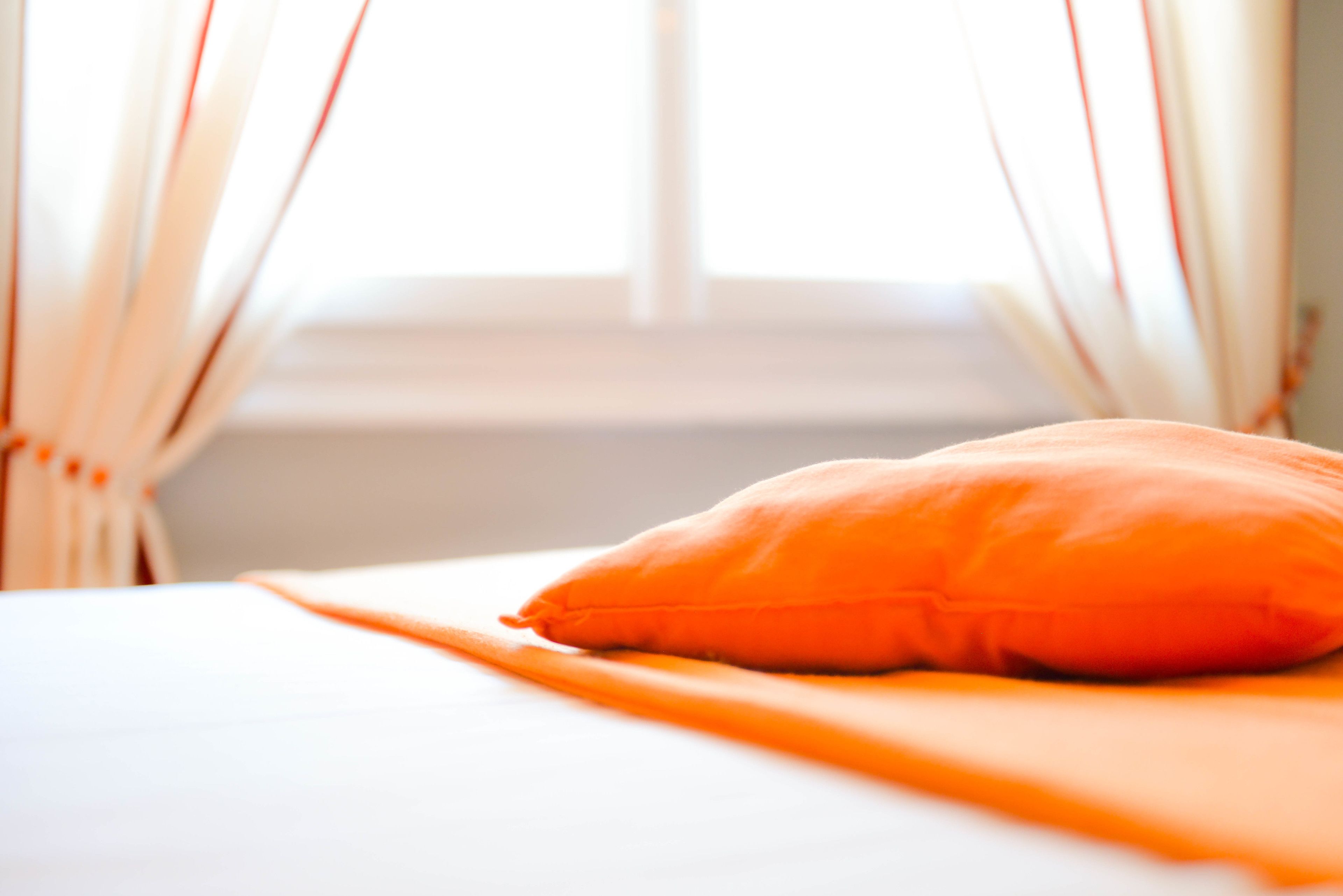 A bed with an orange pillow and white bedding.