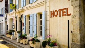 A hotel facade with a sign reading "HOTEL" and a smaller sign for "Logis" indicating a restaurant. There are flower planters along the sidewalk. -  Logis Hôtel Restaurant Résidence (Nissan-lez-Enserune)