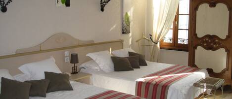 A hotel room with two beds, each with white bedding and red-striped bedspreads. There is a bedside table with a lamp, a wooden headboard, and a window with curtains.