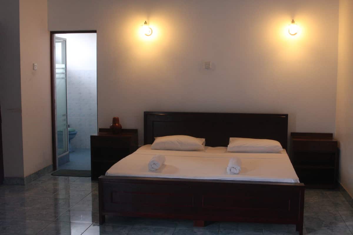 A hotel room with a large bed, two bedside tables, and a door leading to a bathroom.