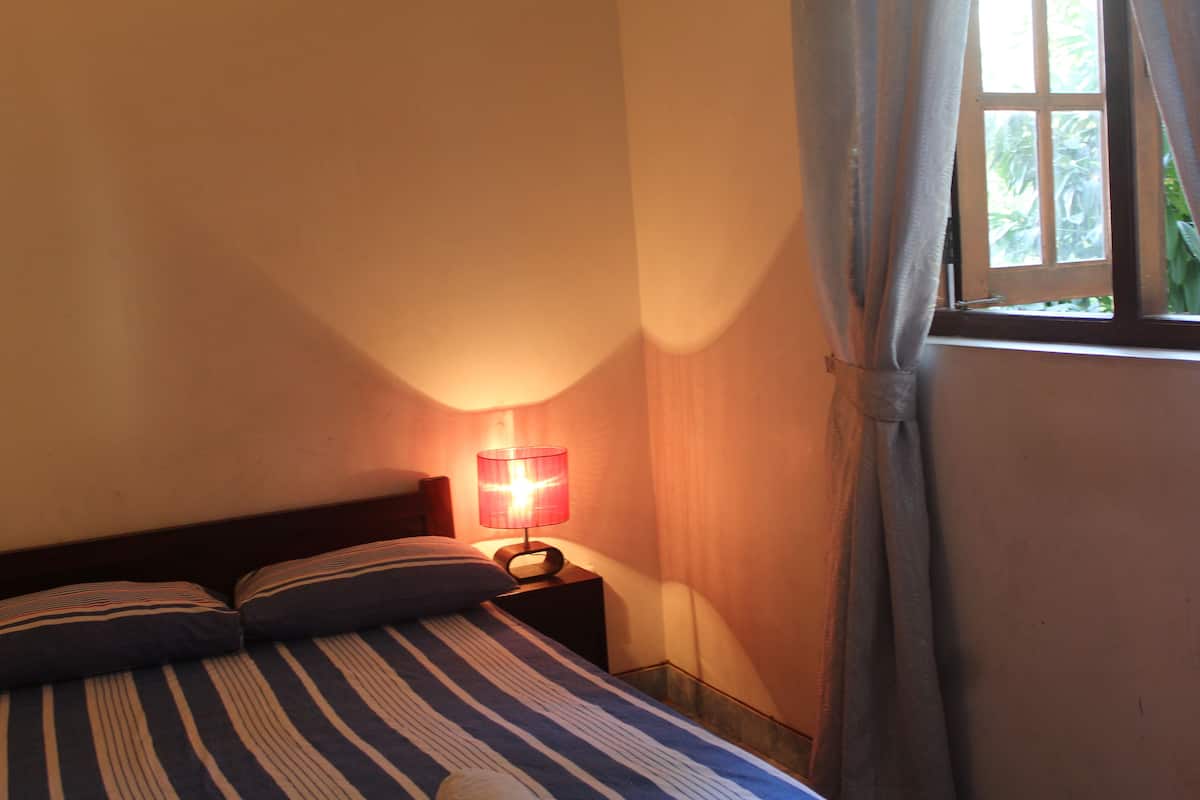A bed with striped bedding, a bedside lamp, and a window with curtains.