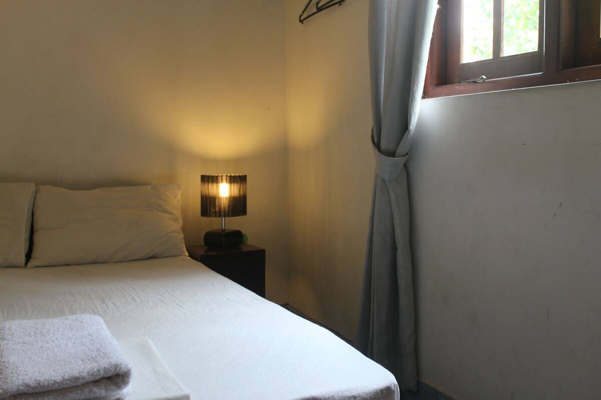 A bedroom with a bed, a bedside lamp, and a window with curtains.